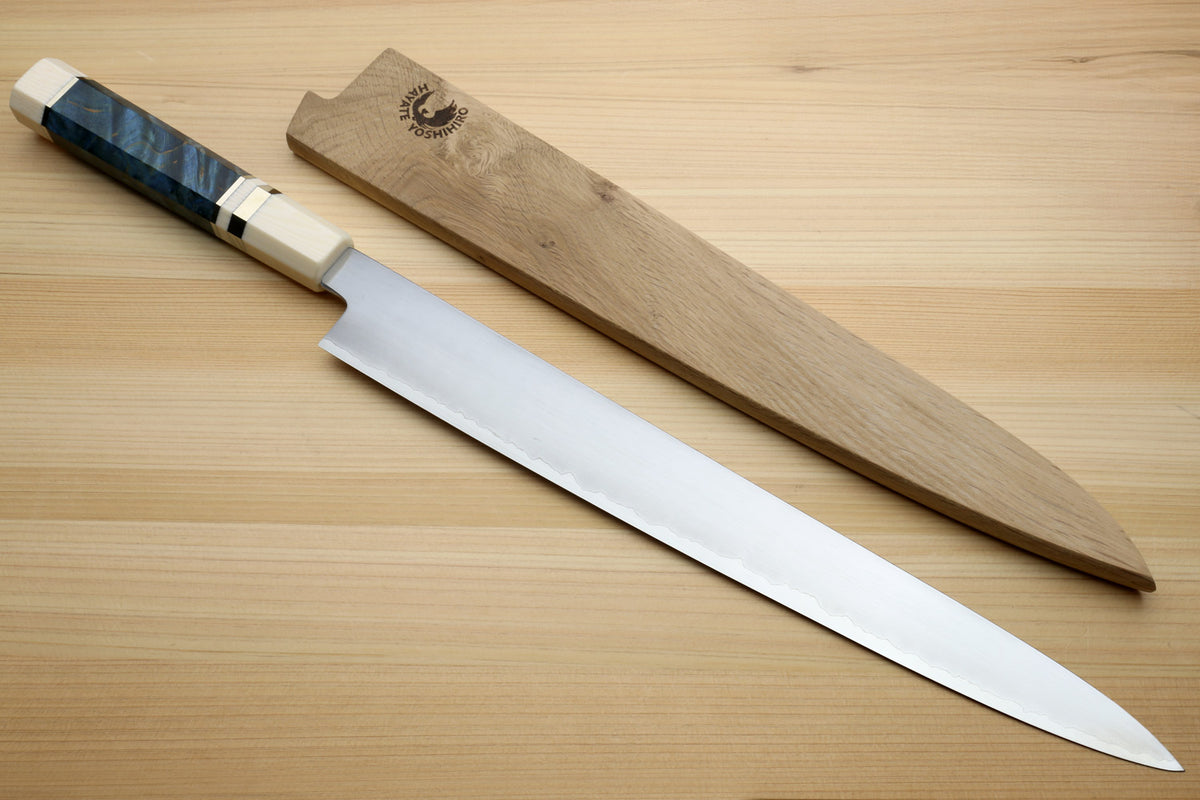 A Japanese-style kitchen knife with a silver blade and a dark blue marbled handle, displayed diagonally next to its wooden sheath on a light wood grain surface.