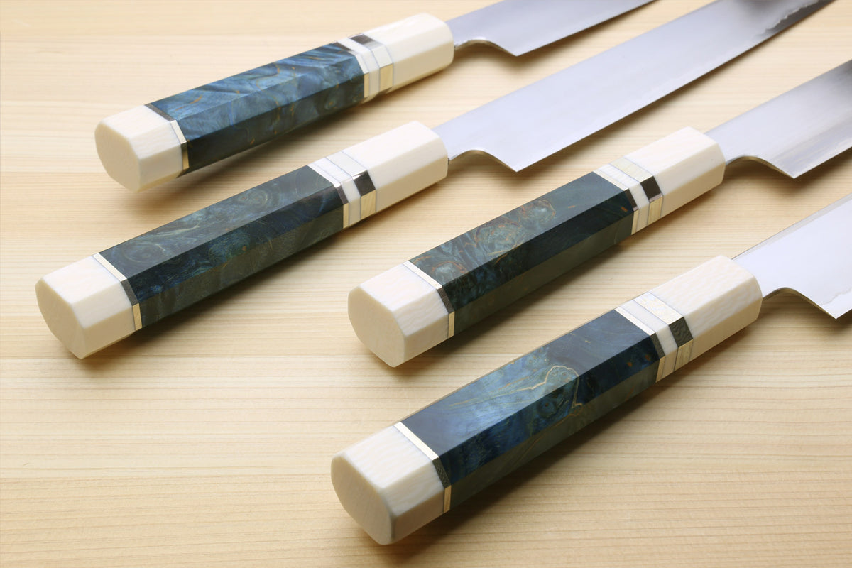 Five Japanese kitchen knives with dark blue and black marbled inlay handles and cream-colored end caps, arranged diagonally on a light wood surface.