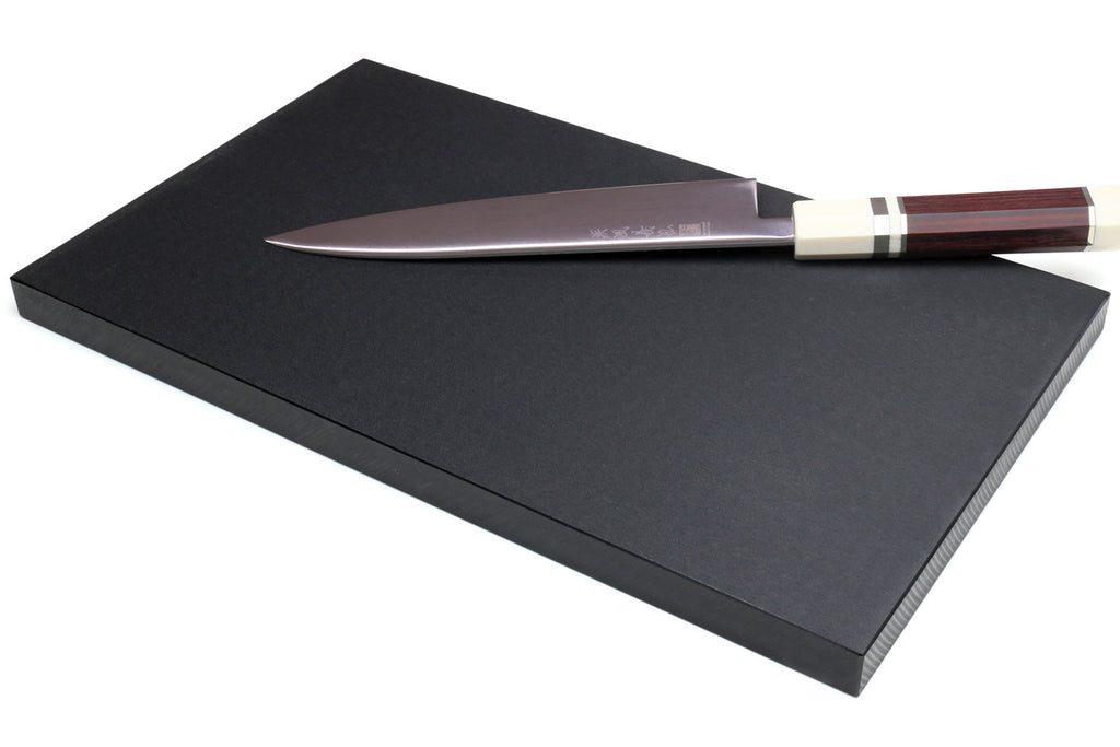 Black cutting board with a chef's knife laid across the surface