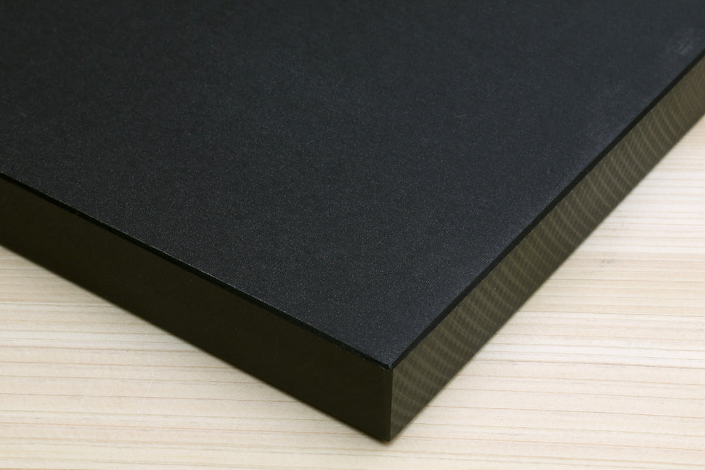 Close-up of a black cutting board corner on a wooden counter, showing its thickness