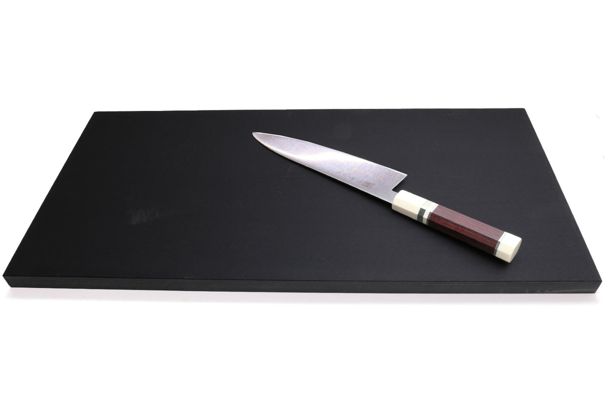 Black cutting board with a Damascus chef's knife resting across the top
