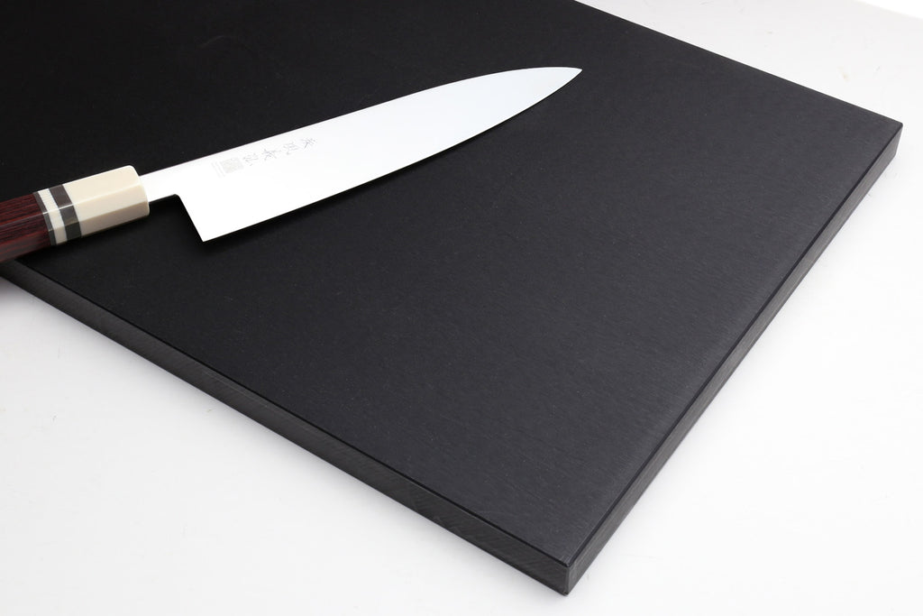 Black cutting board with a Japanese chef's knife resting on one corner