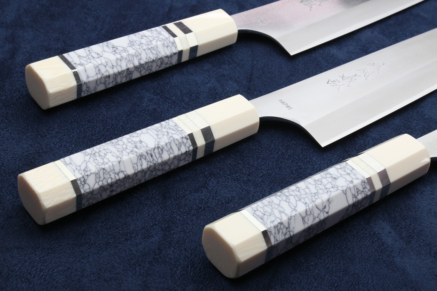 Three knives with white handles and gray patterns on a dark blue background