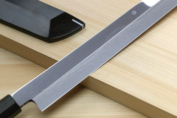 Japanese kitchen knife with silver blade across dark saya on wooden board