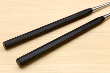 Ebony octagonal handles of plating tweezers with silver metal ends on wood
