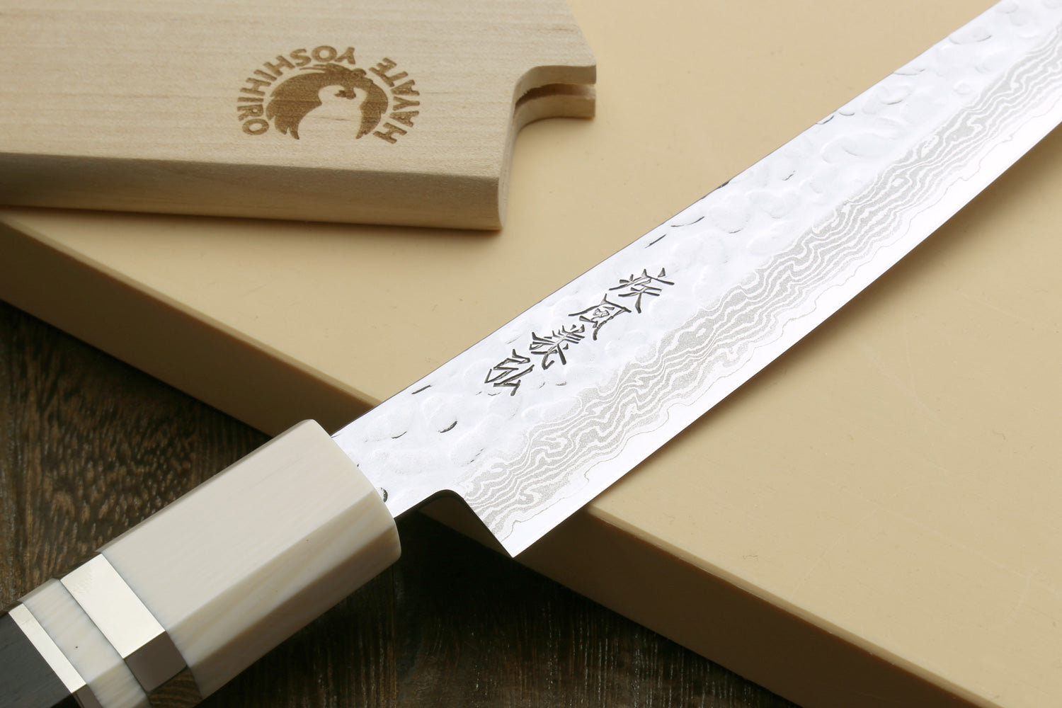 Damascus blade close-up with ivory-look handle and wood display block