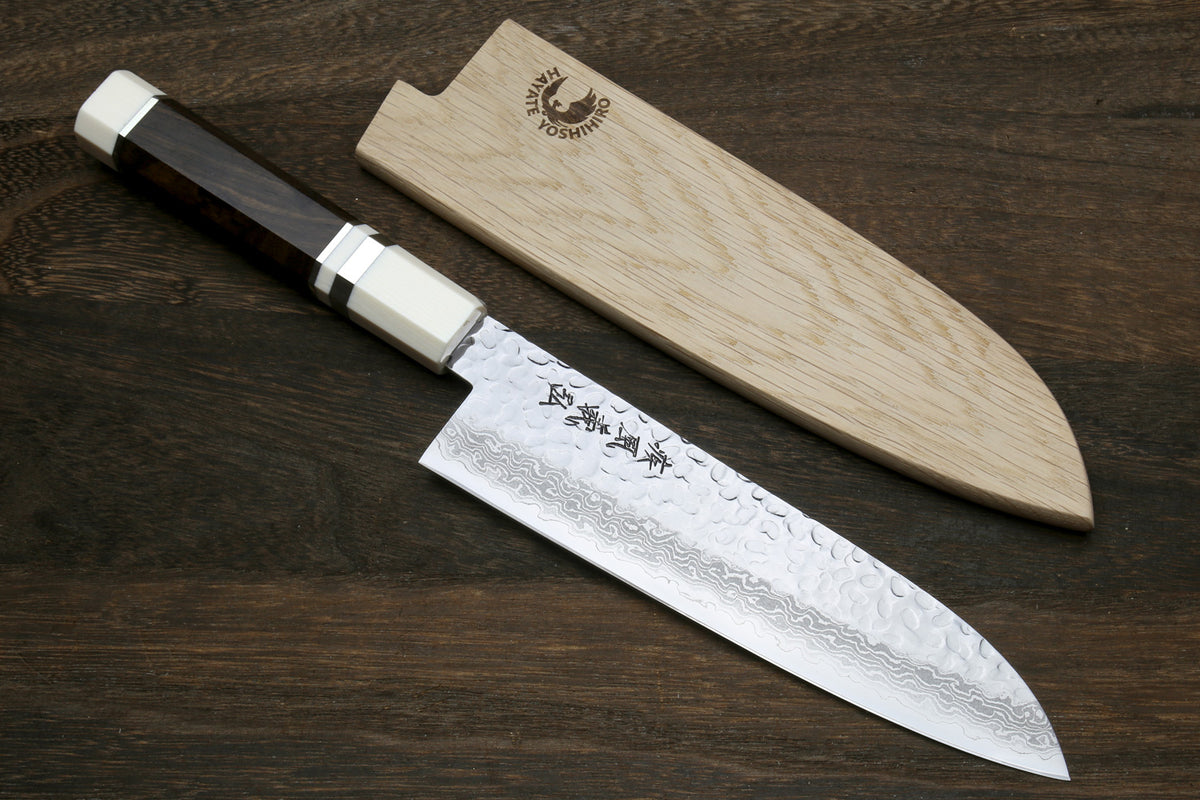 Damascus Santoku knife laid with wooden saya, light octagonal handle and dark blade.