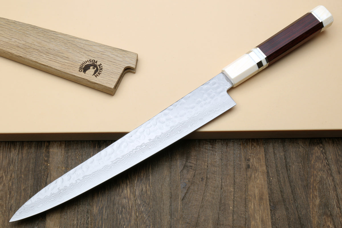 A Japanese-style kitchen knife with a hammered Damascus steel blade, a silver bolster, and a dark reddish-brown wooden handle, shown alongside its matching wooden sheath on a beige background with a dark wood surface below.