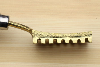 Gold metal fish scaler head with serrated teeth, shown in close-up
