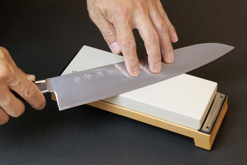 Knife being sharpened on a whetstone, white stone on wooden base with hands