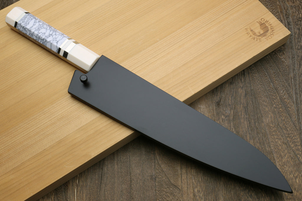 Chef's knife with a white handle stored in a wooden sheath on a wooden cutting board