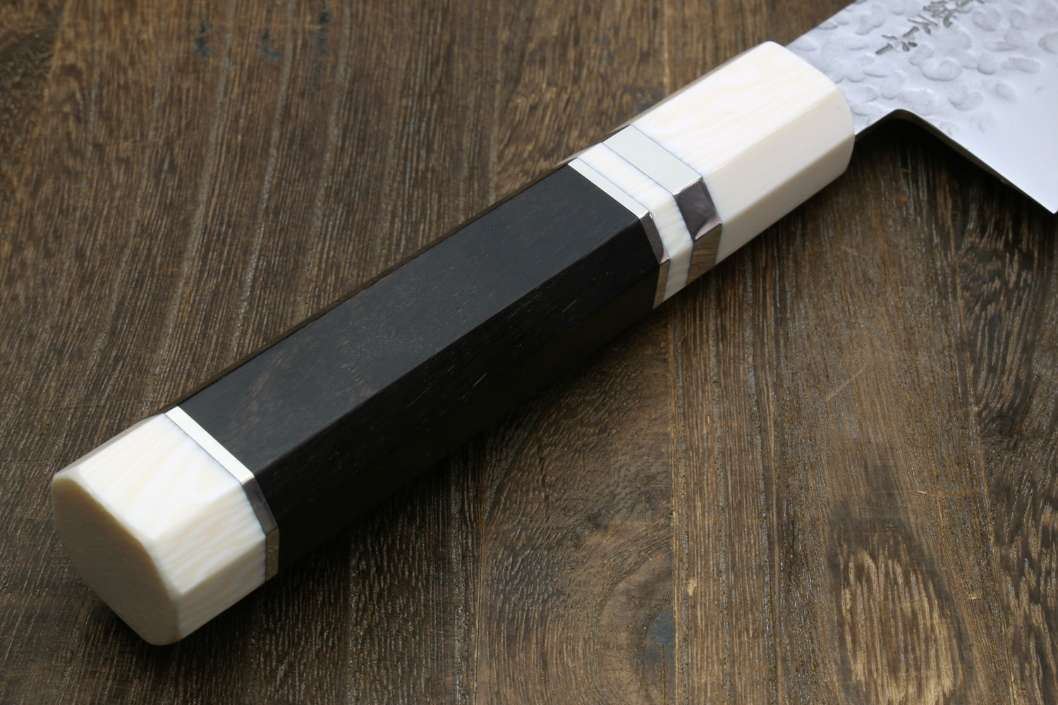 Close-up of a knife with a ebony wood handle with white alternative ivory bolster on a wooden surface