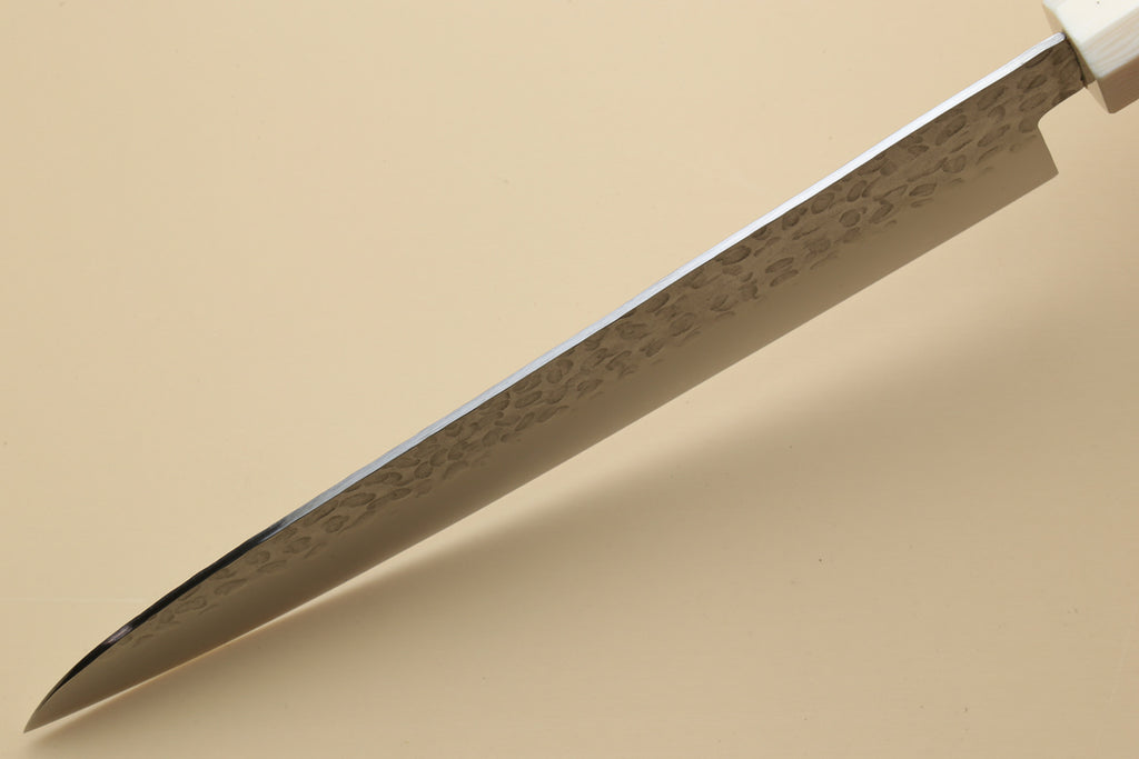 Chef's gyuto knife tip close-up with hammered stainless steel blade and ivory bolster