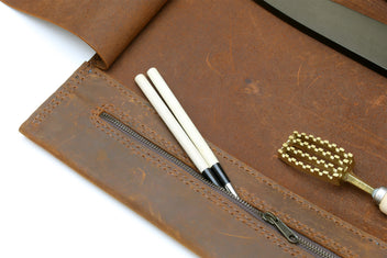Brown leather knife roll case with tools and knives laid into interior pockets