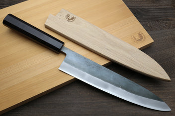 Chef's gyuto knife with black handle and blue steel blade on cutting boards