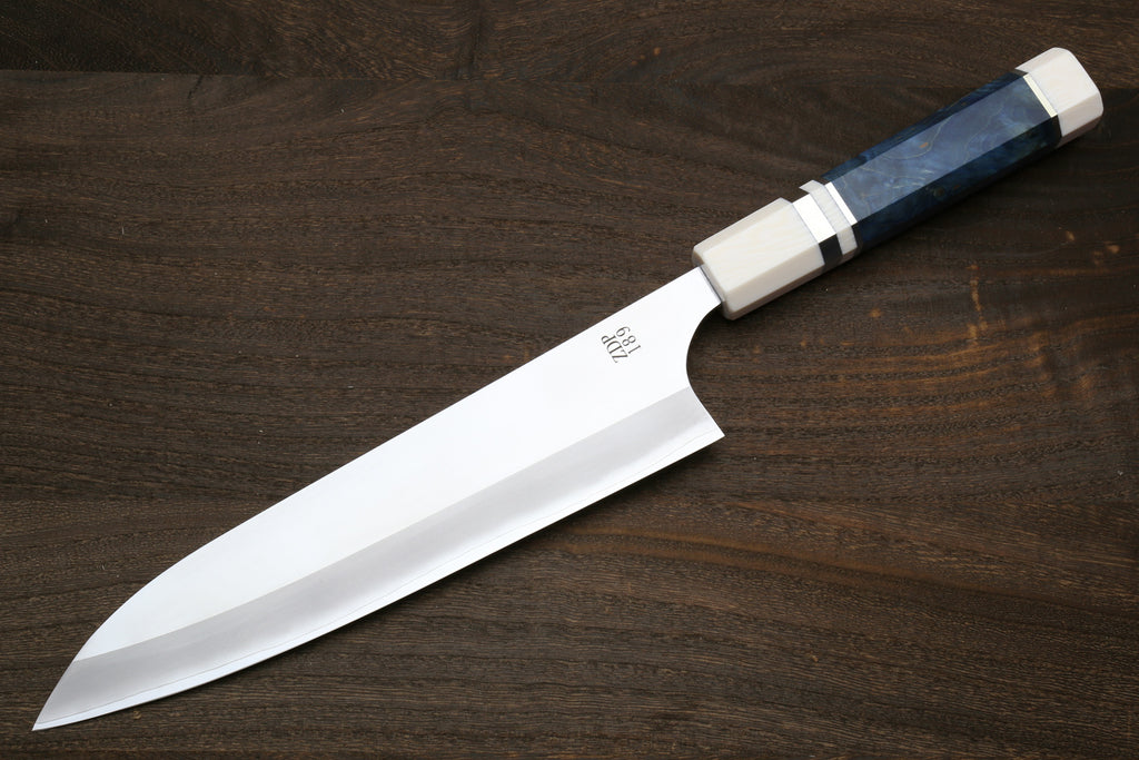 A Japanese-style chef's knife with a polished silver blade and a handle made of dark blue lapis lazuli, resting diagonally on a dark wood background.