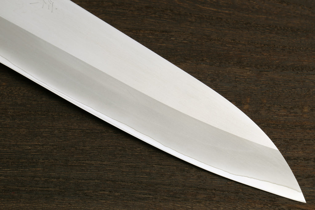 A close-up of a polished steel knife blade resting diagonally on a dark brown wood surface.