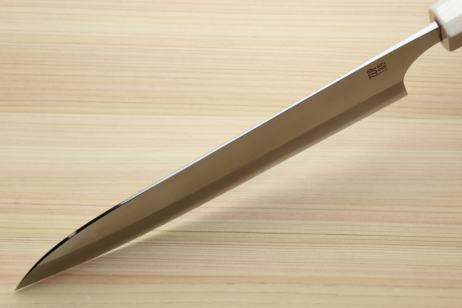 A stainless steel kitchen knife with a white handle, shown diagonally on a light wood grain surface.