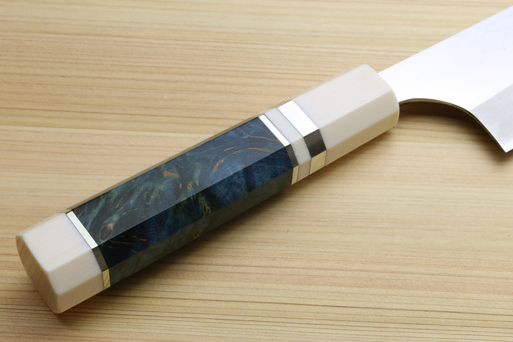 A close-up of a Japanese-style kitchen knife with a curved silver blade and a textured handle made of dark blue and black marbled material with cream-colored end caps, resting on a light wood grain surface.