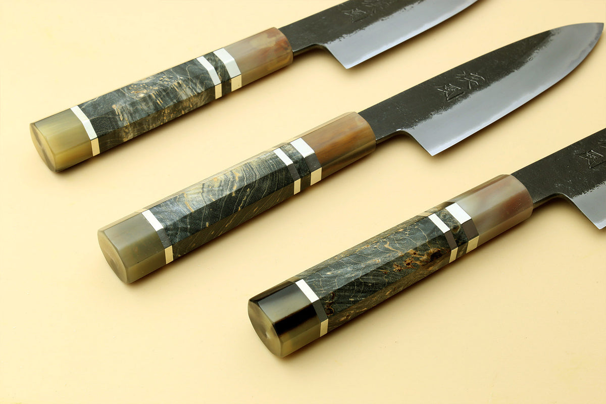 Set of paring knives with dark handles and silver blades, one showing stamped logo.