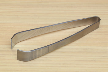 Stainless steel tweezer with extended V-shaped jaws on wooden board