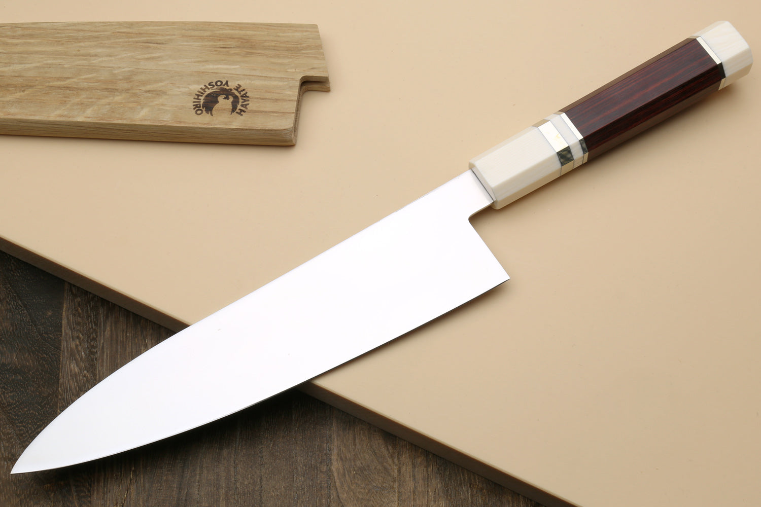 A chef's knife with a polished silver blade and a dark brown wooden handle with cream-colored end caps, resting diagonally on a beige background with a wooden cutting board partially visible in the top left.