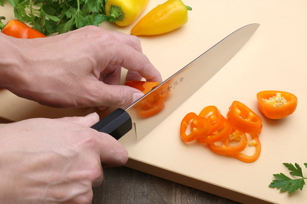 Person slicing orange bell peppers on a cutting board with a knife.