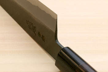 Chef knife with dark D-shaped handle and blackened blue steel blade heel close-up