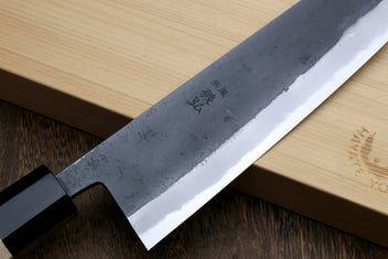 Blue steel gyuto knife blade with etched markings, kurouchi texture, black handle collar