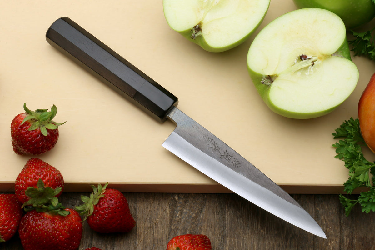 Kitchen knife with a black handle and silver stainless blade on a cutting board.