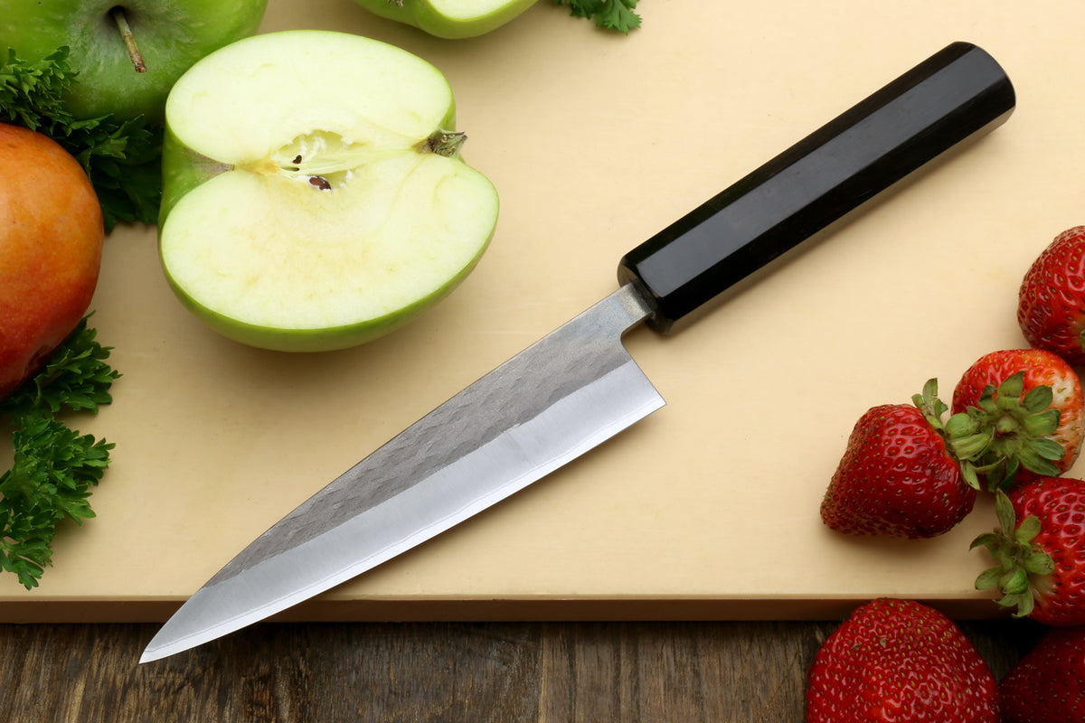 Kitchen knife with a black handle and silver stainless blade, angled on a board.