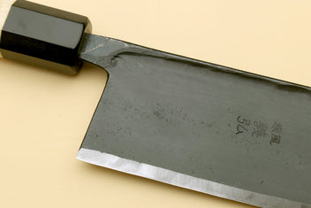 Nakiri vegetable knife close-up: dark steel blade with etched markings, black bolster