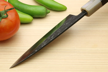 Petty utility knife angled on board with dark handle and gray patterned blade