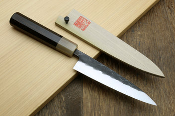Petty utility knife on wood with black handle and gray patterned blade