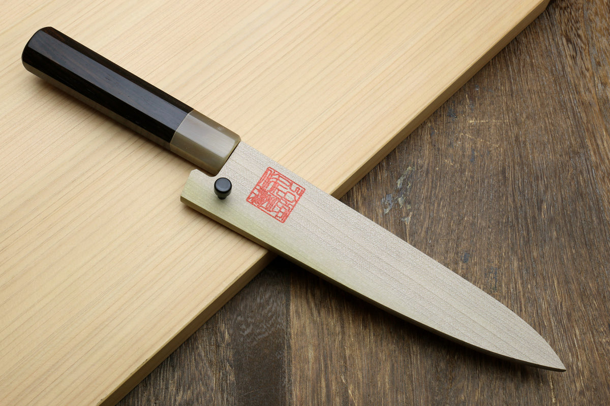 Petty utility knife on wood with black handle, silver bolster, and gray blade