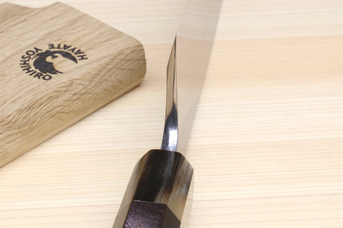 Deba knife side view with white blade and dark handle on wooden block