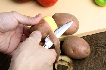 Paring knife with dark brown wood handle shown in hand, hammered Damascus blade