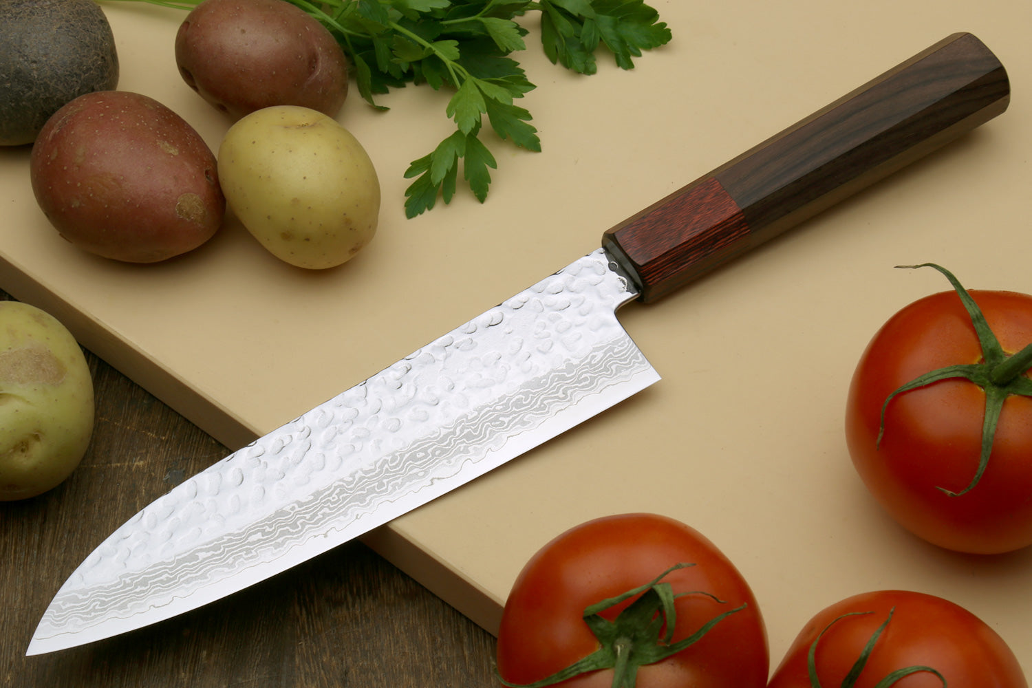 Hammered Damascus santoku knife with octagonal dark wood handle, blade angled on board.