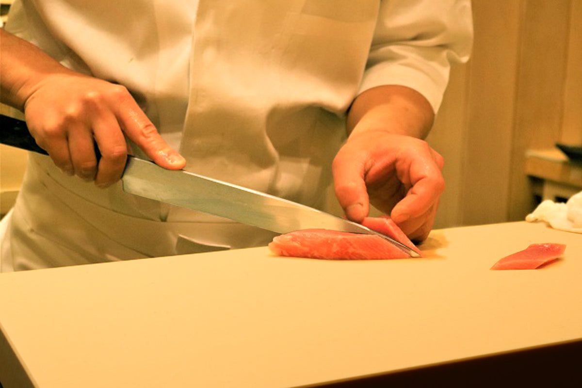 Japanese cutting board with sliced fish pieces and chef hands preparing food.