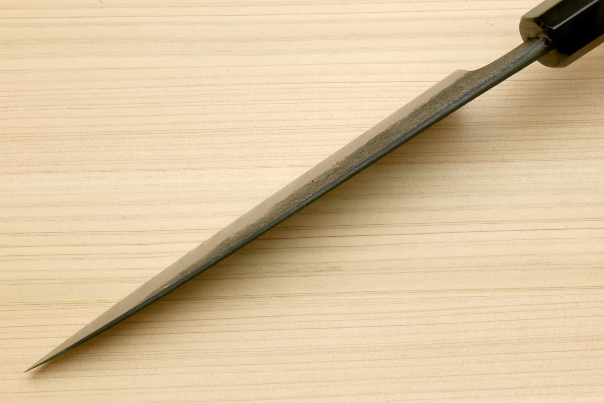 Japanese petty utility knife with pointed blade and dark bolster near handle