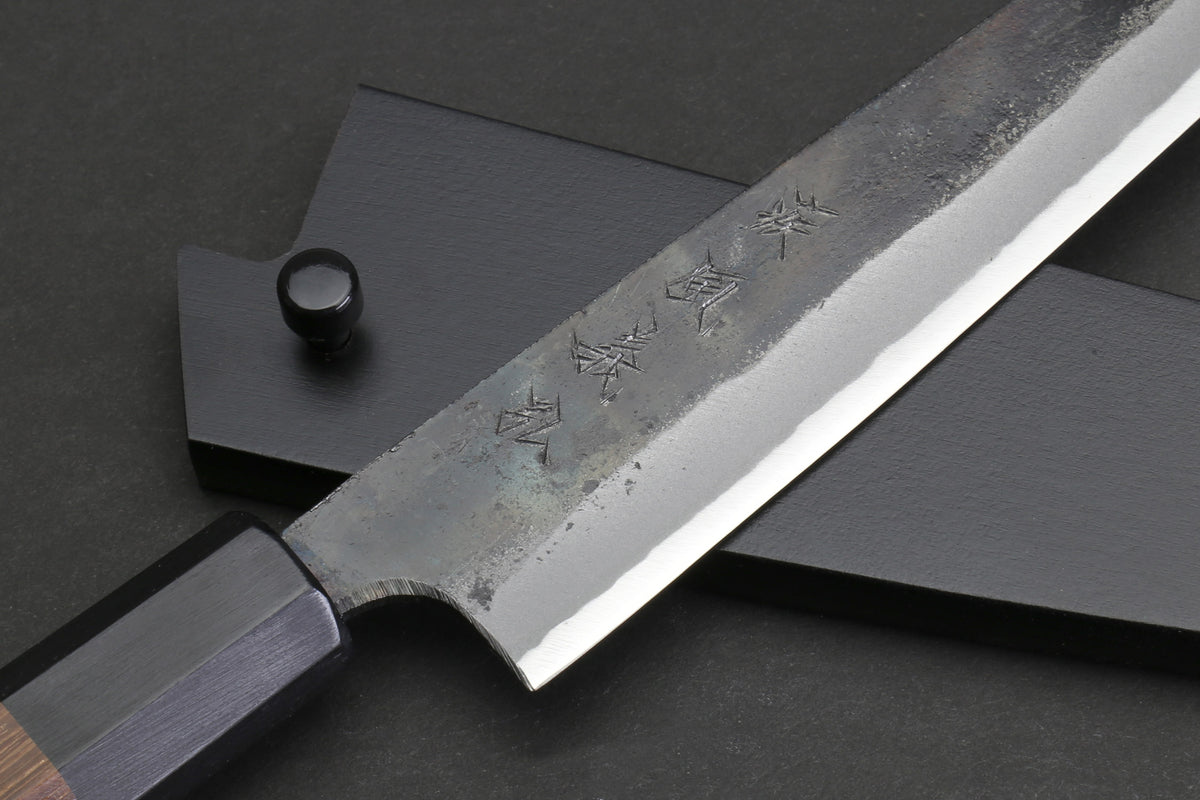 Kurouchi-finished steel petty blade with engraved characters and dark handle end.