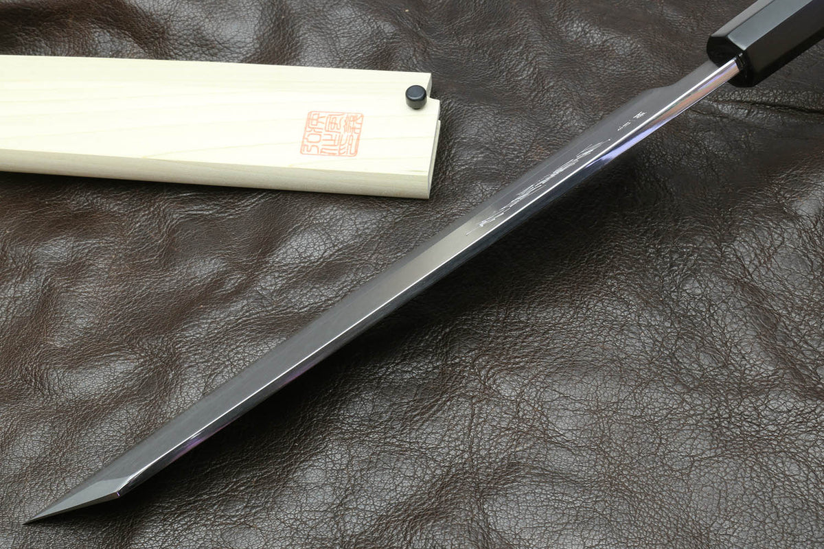 Multipurpose chef knife with silver blade and black handle beside light wood sheath