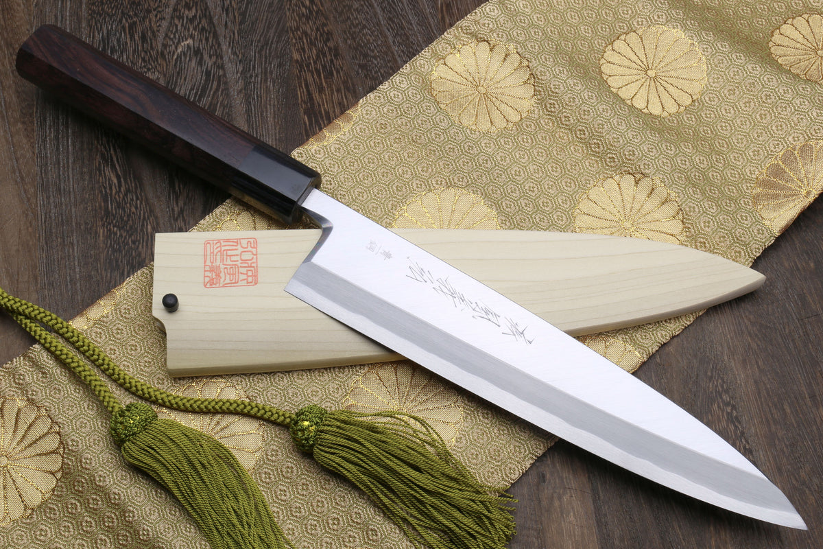Japanese chef knife with light saya, dark handle, and green cord