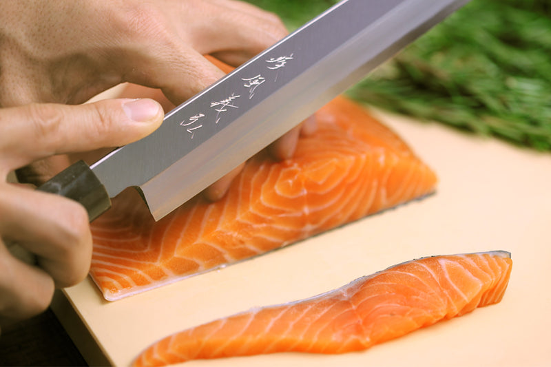 Cream cutting board with salmon fillets being sliced with a chef’s knife