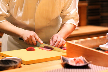 Cook preparing food on a beige cutting board with a knife and fresh produce nearby
