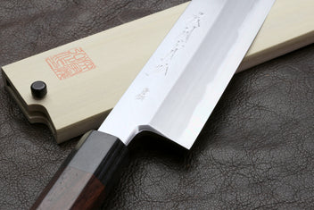 Japanese chef knife with pale blade and saya, dark handle, on leather