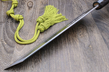 Japanese chef knife with white steel blade and magnolia handle, laid on green tassel cord.