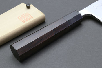 Deba sushi fillet knife with dark handle and light wooden saya on wood support