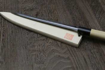 Sashimi filet knife with silver blade resting in light wood saya, black bolster