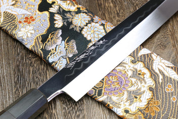 Yanagi knife blade close-up with mirror edge on gold and black patterned fabric